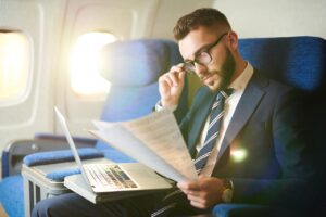 Businessman traveling on airplane reading documents and having a laptop open on his tabletop