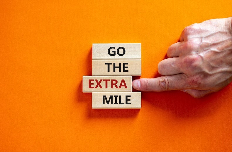 Go the extra mile symbol. Wooden blocks with words 'Go the extra mile'. Male hand. Beautiful orange background. Business and go the extra mile by Sobirovs Law Firm