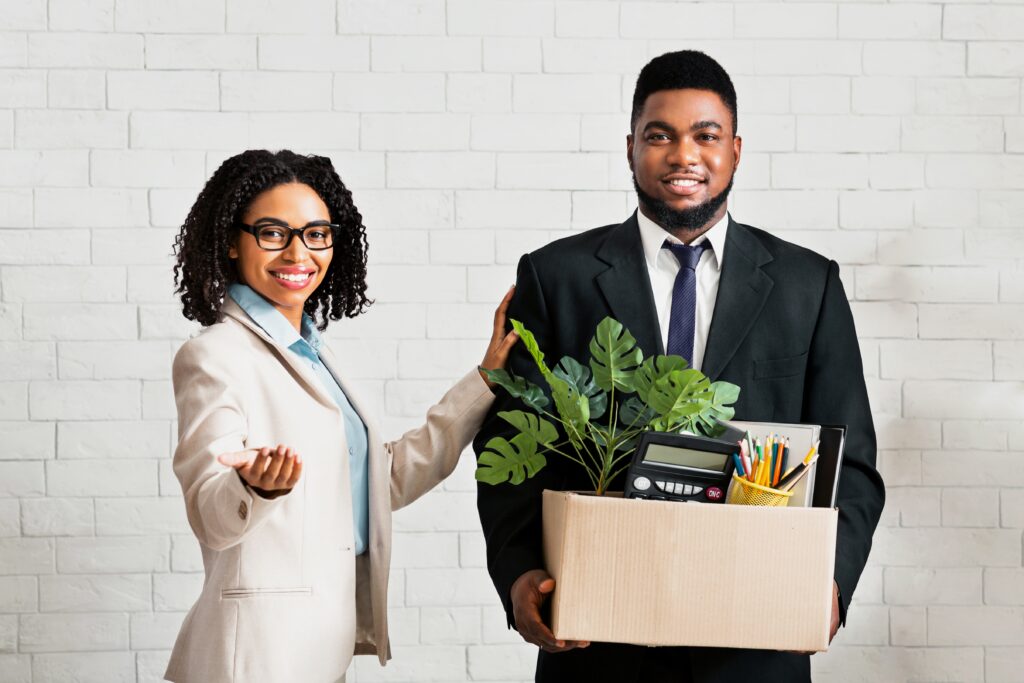 Professional woman welcoming a new employee carrying office supplies in a box, representing the successful integration of individuals who have completed the C11 work permit process and achieved their goal to benefit Canada through chemical financial services expertise, demonstrating cultural benefits as they establish their own business operations and contribute to the Canadian economy while maintaining supporting documents and financial records required for their business immigration status.
