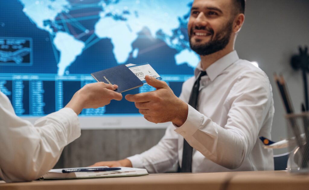 Smiling immigration consultant handing a passport to an international student in front of a world map display, representing the successful completion of their Express Entry profile and transition from a student visa to Post Graduation Work Permit, with their common law partner and dependent children preparing to enter Canada legally through the Federal Skilled Trades Program, while considering initial living expenses, prescription drugs coverage through private health insurance, Canadian education opportunities at a Canadian institution, and innovative business ideas for the Start Up Visa Program, all while navigating tax law requirements and the permanent residence fee as they work toward Canadian citizenship in British Columbia through the Comprehensive Ranking System and temporary resident permit processes.