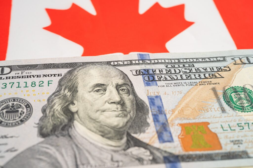 A US one hundred dollar bill positioned against the Canadian flag's maple leaf, symbolizing the financial considerations for those seeking family sponsorship and temporary work permits, including language skills assessment fees, health insurance coverage requirements, and the transition from temporary resident permit status while navigating business immigration pathways and ensuring proper documentation to enter Canada through the immigration system.