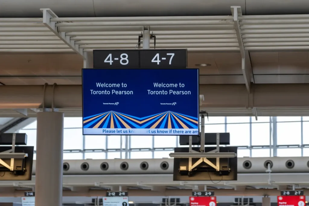An electronic sign at an airport displays Welcome to Toronto Pearson above colorful lines and gate numbers 4-8 and 4-7—a perfect first impression for those buying a franchise in Canada.