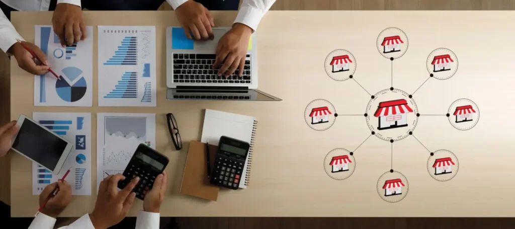 Four people work at a desk with graphs, charts, and devices. On the right, a diagram shows a central store linked to smaller stores, symbolizing buying a franchise in Canada and building a successful business network.