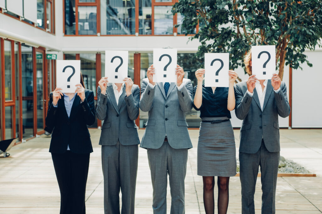 Several foreign nationals hold question marks, symbolizing confusion around who can apply for open work permits in Canada, including dependent spouses, recent graduates, and temporary foreign workers.