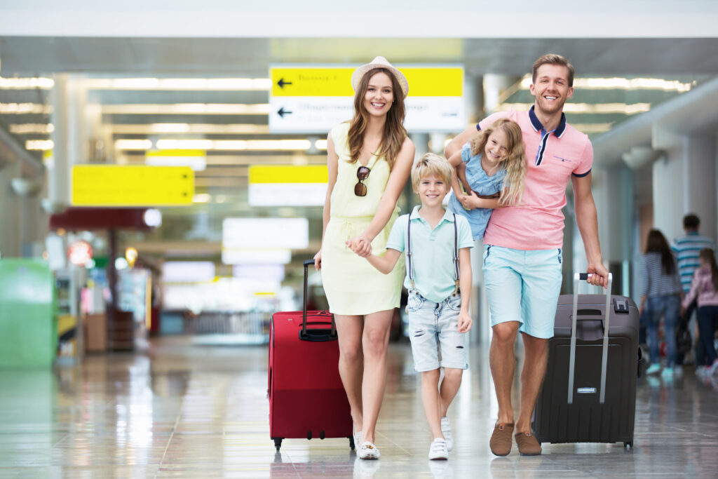 A smiling family holding a Canadian flag and luggage at an airport terminal, symbolizing their move from the U.S. to Canada.