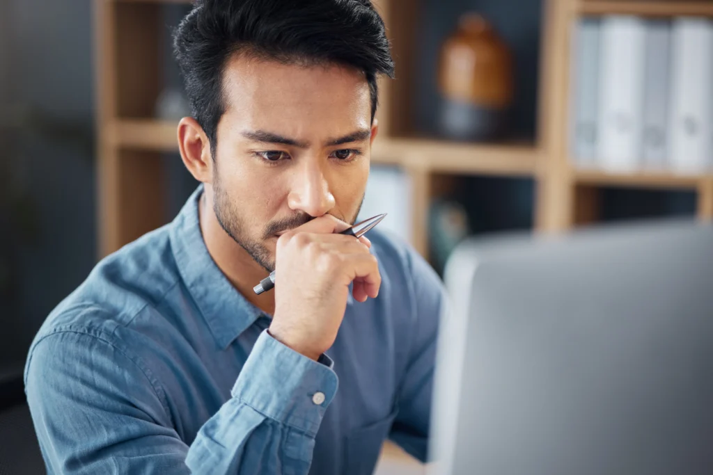 A man intently looking at his computer screen while researching Canadian immigration programs, symbolizing the importance of understanding PR obligations under the PNP.
