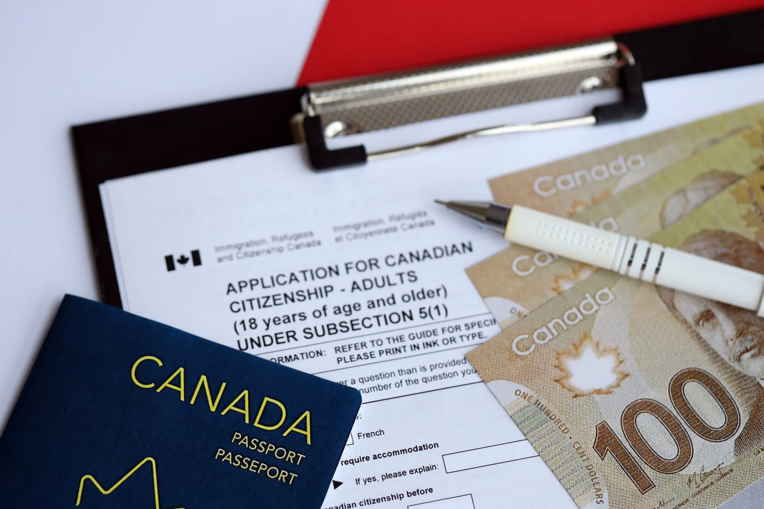 Immigration documents, application checklist, and pen on table with Canadian flag in background