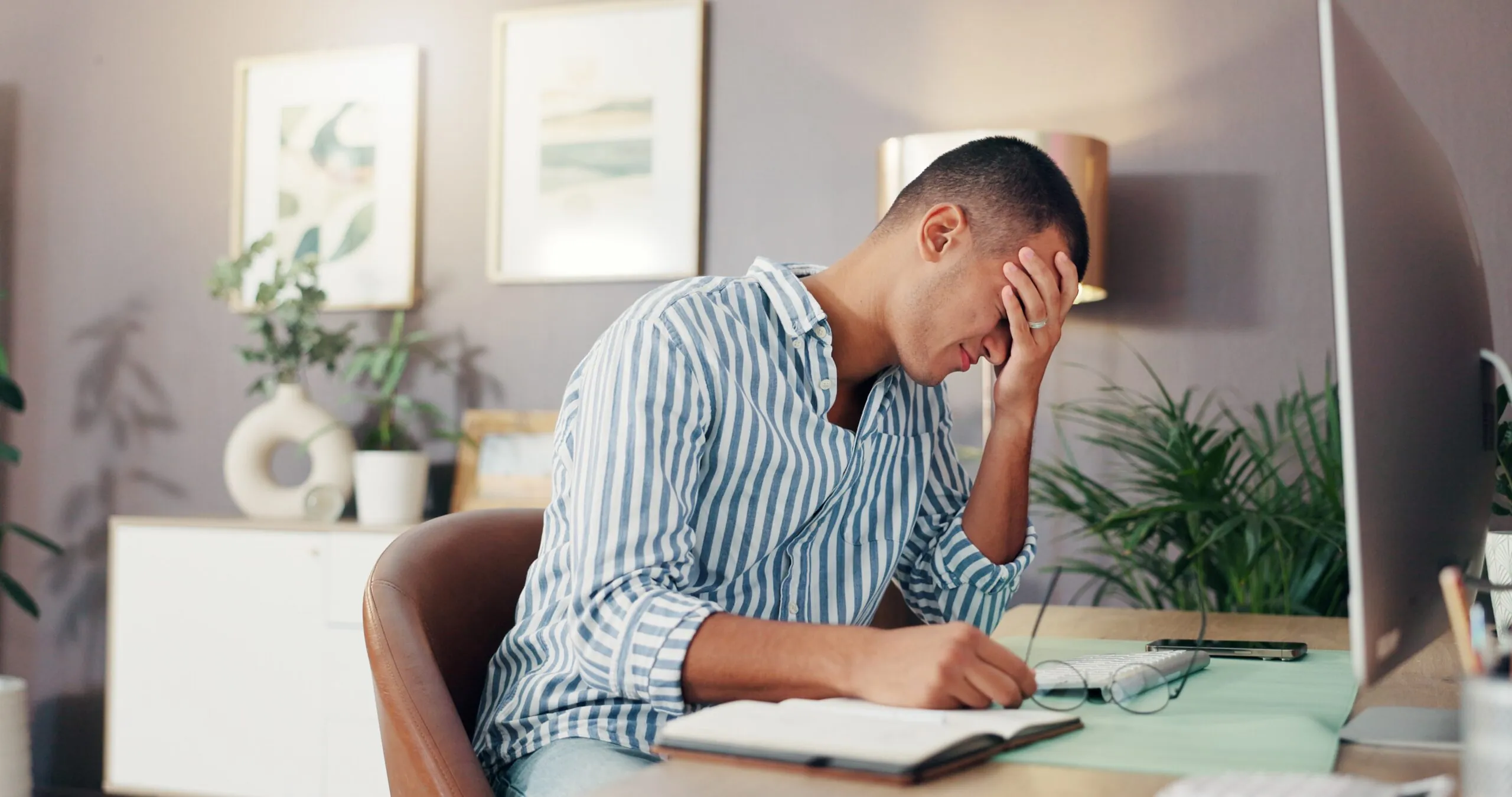 Frustrated entrepreneur holding his head in his hands while reviewing documents at his desk, representing the stress experienced by applicants facing challenges in the start up business class immigration process under Immigration and Refugee Protection regulations, dealing with peer review complications and visa officer decisions that affect their immigration status, while working through the complex process that IRCC announced for start up applications, requiring thorough business activity documentation and innovation plans to secure the necessary letter and avoid having their entire group's application impacted by common bureaucratic challenges in the application process.