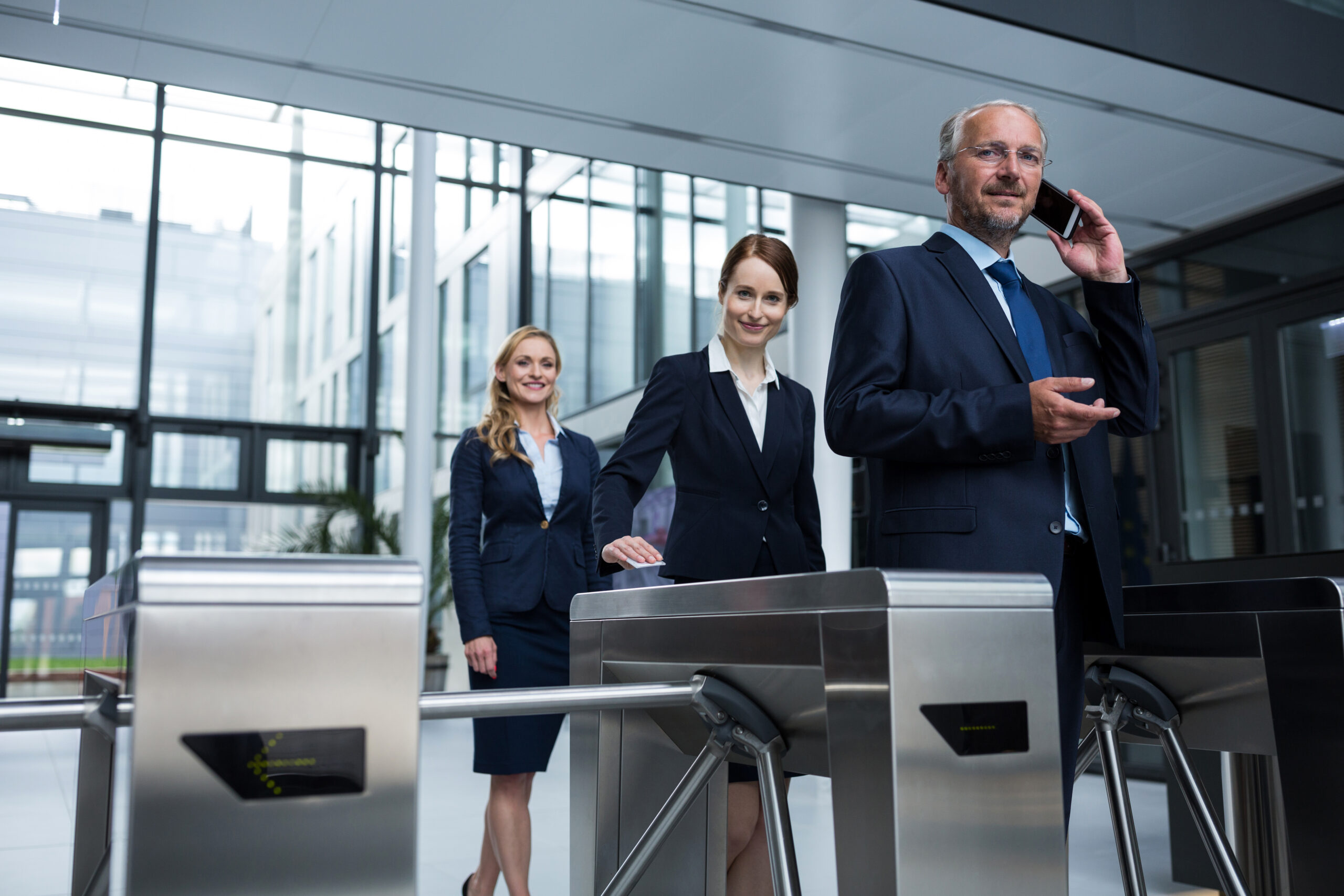Business executives at security turnstiles in a corporate building, with one professional on a phone call, representing business visitors and foreign nationals coordinating with Social Development Canada and Citizenship Canada regarding work permits and consular processing, while their law firm handles compliance reviews and assists with the federal immigration process to ensure proper documentation for business travel and global mobility within Canada's immigration system.