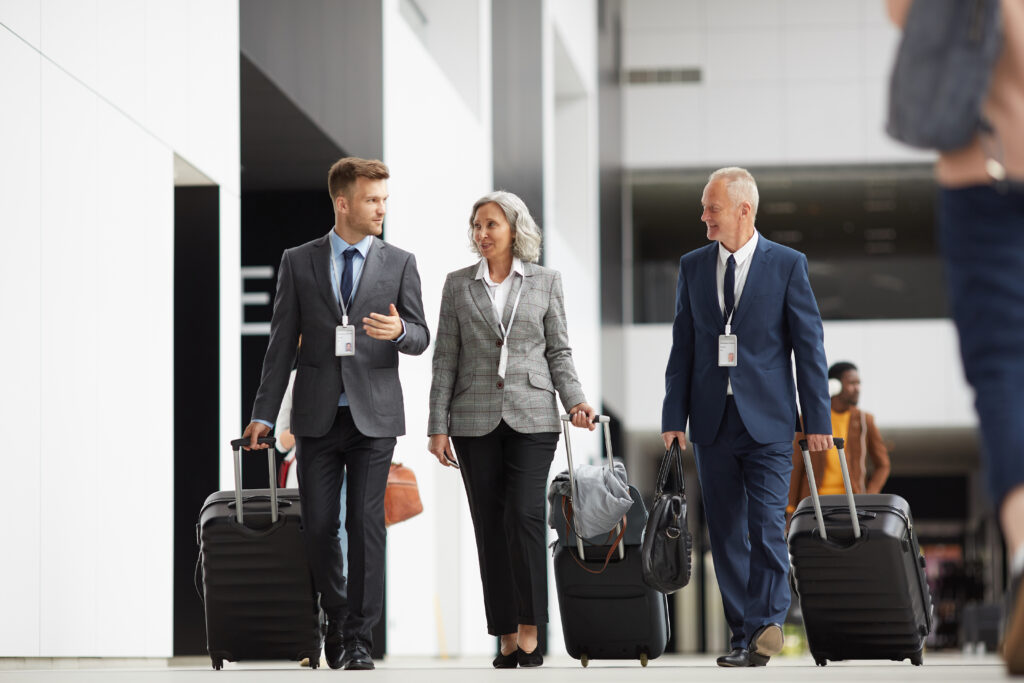 Three business travelers with luggage walking through an airport or transit facility wearing identification badges, representing skilled workers and business visitors navigating the immigration process with assistance from immigration lawyers who specialize in Canadian work permits, business immigration applications, and compliance reviews, ensuring foreign nationals meet federal regulations for global mobility while their law firm coordinates with Citizenship Canada and handles consular processing requirements for successful entry to Canada.
