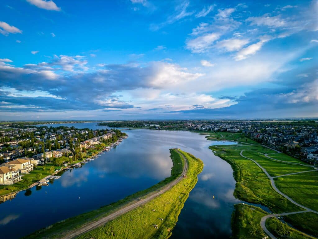 Aerial view of a river with a green peninsula dividing the water, surrounded by residential houses—an ideal setting for an AAIP rural entrepreneur stream lifestyle amid lush grass and a dramatic blue sky with scattered clouds.