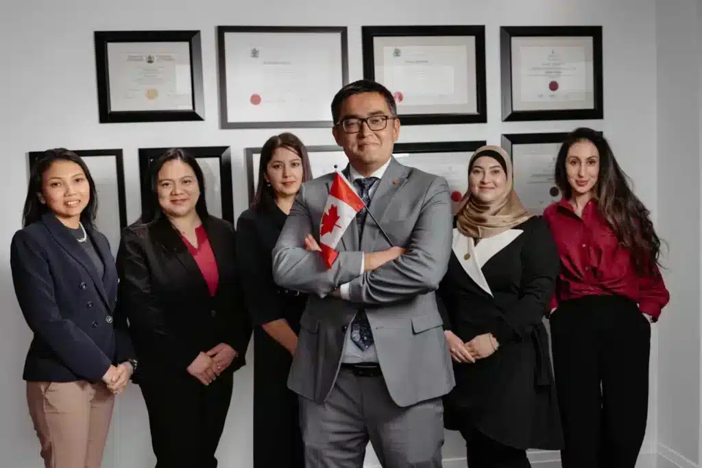 Sobirovs business immigration lawyers in Toronto posing with Canadian flag in office, diplomas on wall behind.